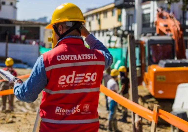 Edeso, imagen que muestra a un contratista de espaldas, con chaleco rojo de Edeso, está en una obra, usa casco de protección, medición de un topógrafo con estación total.